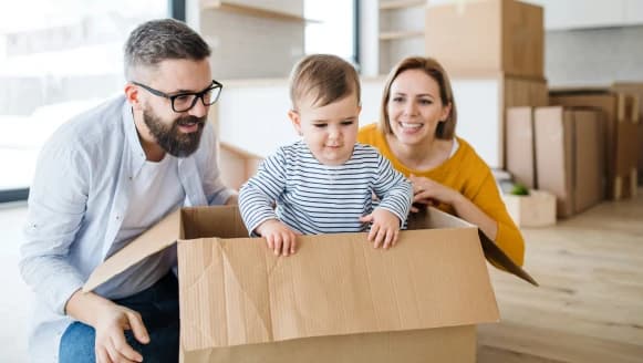 A baby playing in a moving box while family unpacks their new home
